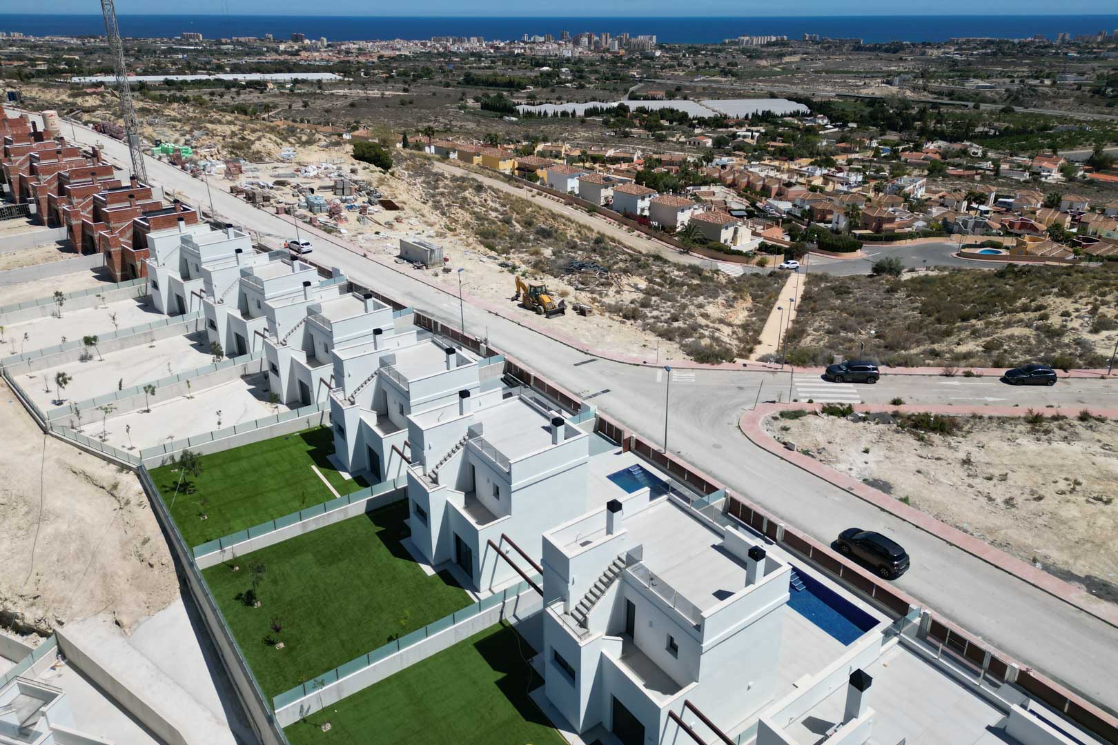 Aerial perspective of modern villas with private lawns, individual pools, and flat roof terraces, situated on an elevated ridge overlooking the Mediterranean coastline.