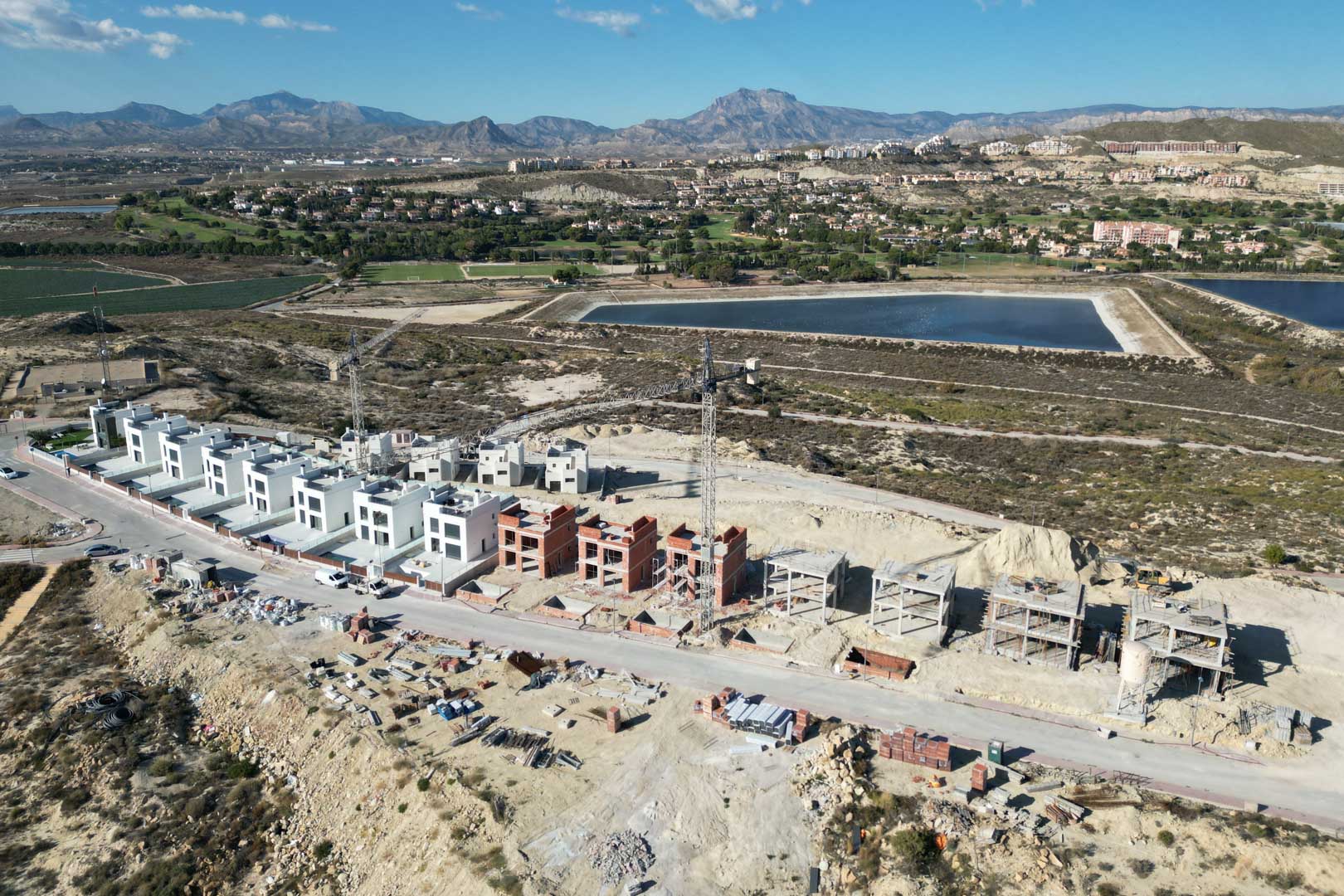 Aerial perspective of the residential project under construction, highlighting villas in different stages of development set within a mountainous landscape.
