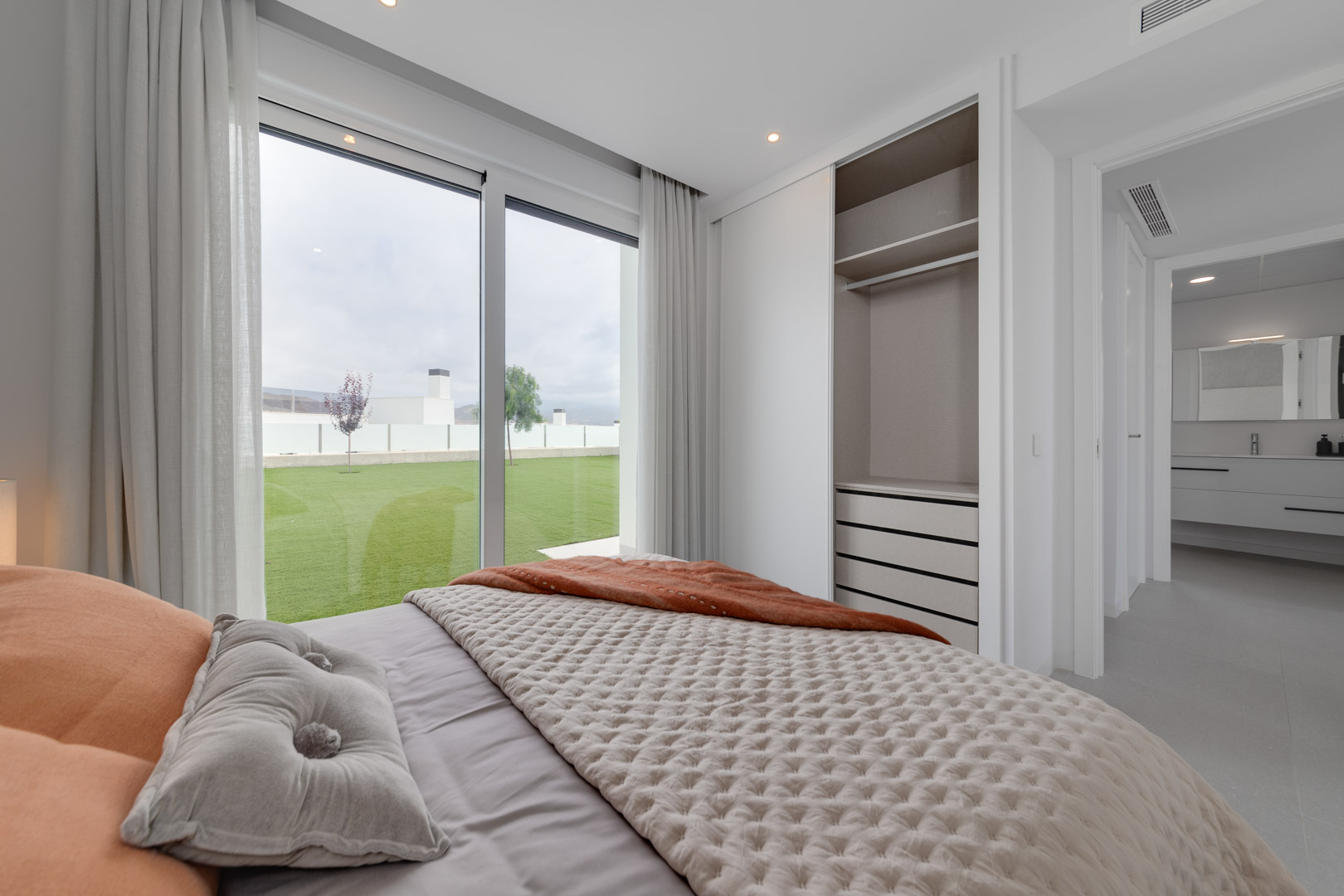 Bedroom featuring a built-in wardrobe with sliding doors, floor-to-ceiling windows with garden access, and a view into the en-suite bathroom.