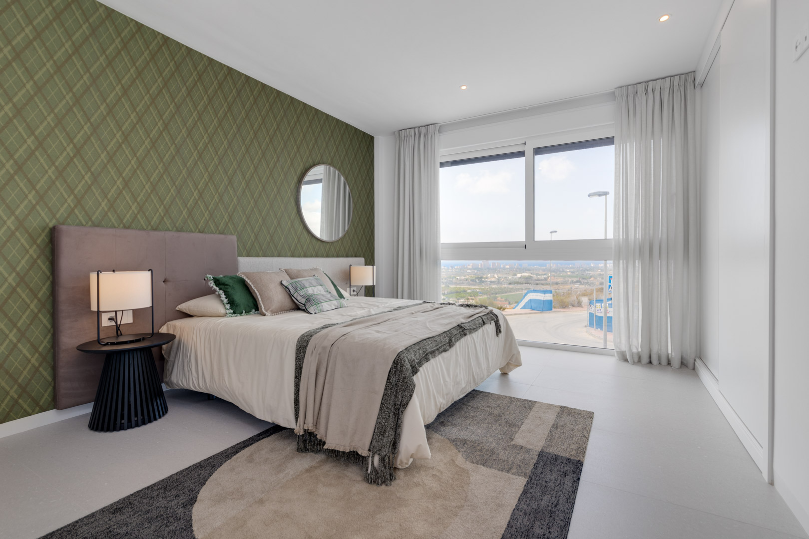 Bedroom featuring a green patterned accent wall, floor-to-ceiling window with panoramic views, and built-in white wardrobes. Modern lighting and neutral tiled flooring.