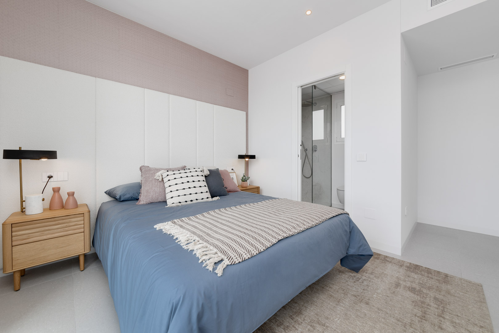 Contemporary bedroom featuring a white paneled headboard, mauve accent wall, and an integrated en-suite bathroom with a glass partition.