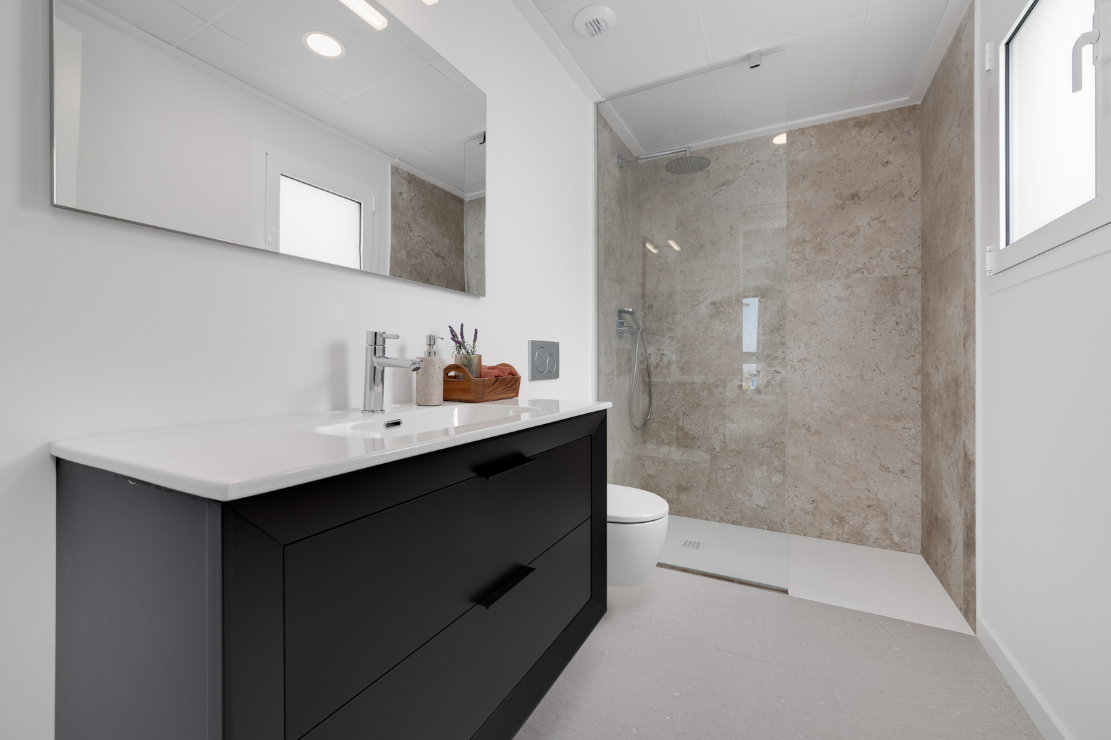 Modern bathroom featuring a black vanity cabinet, walk-in shower with stone-textured tiling, and sleek chrome fixtures.