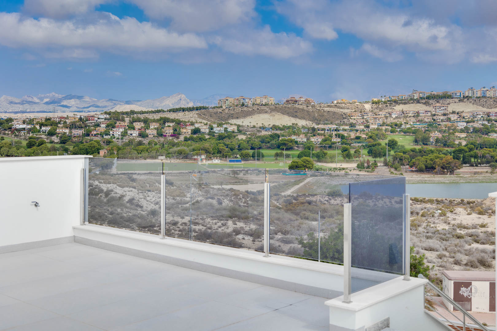 Upper terrace featuring large-format grey tiling and glass balustrades, providing panoramic views of the mountains, local lake, and golf courses.