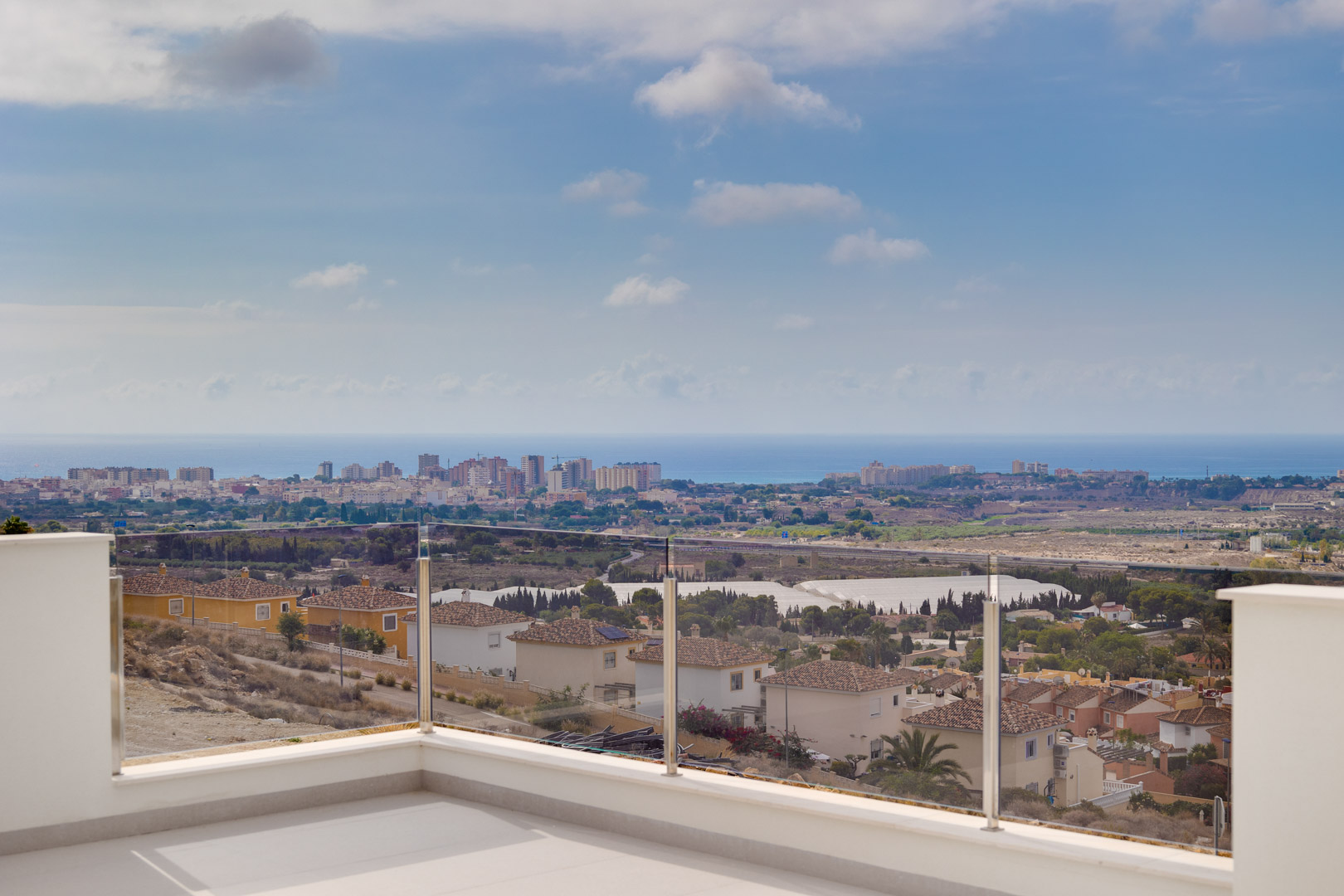Upper terrace featuring light ceramic flooring and a glass balustrade, providing unobstructed panoramic views of the coastline and Mediterranean Sea.