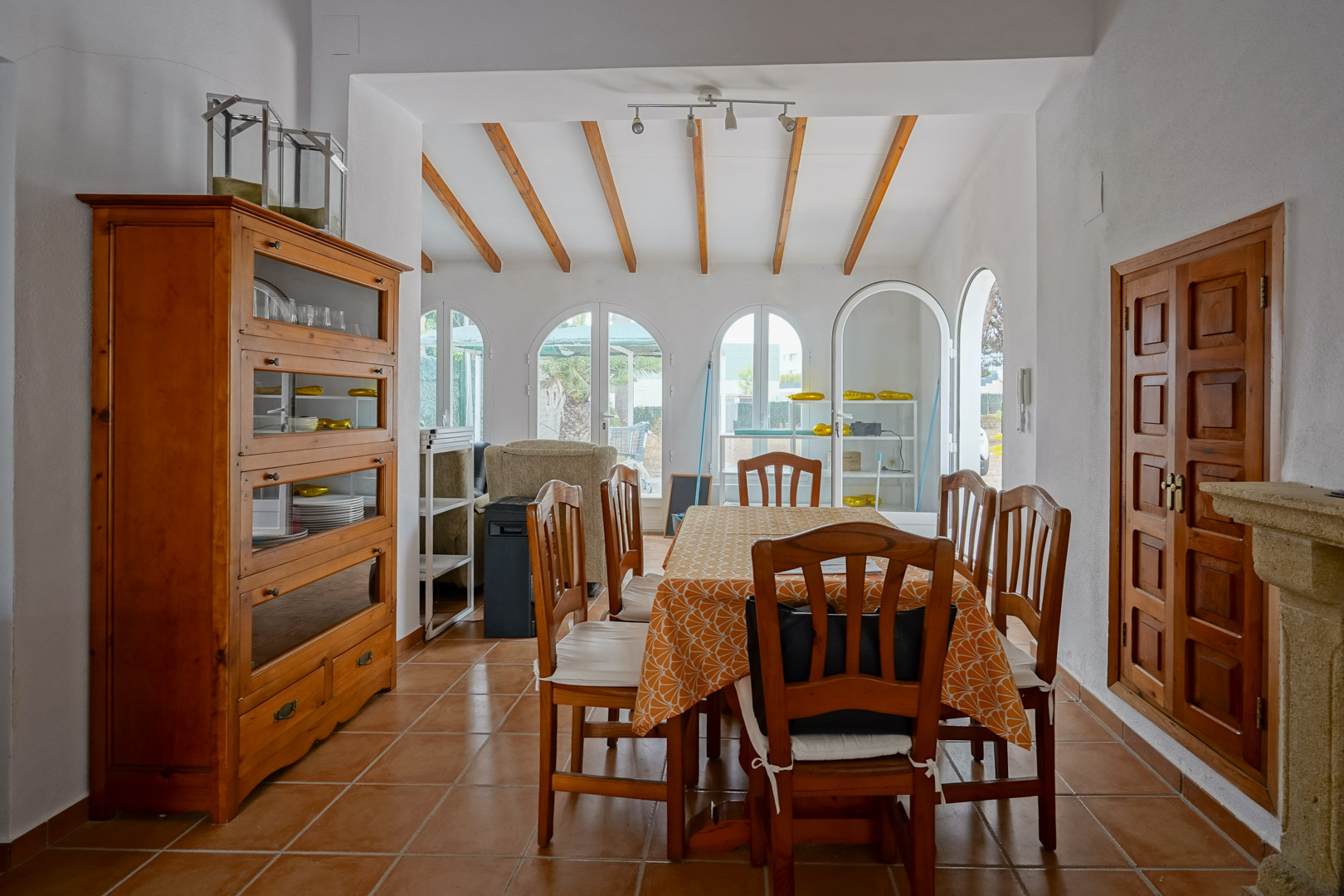 Dining area featuring exposed wooden ceiling beams, terracotta tile flooring, and arched glass doors providing abundant natural light.
