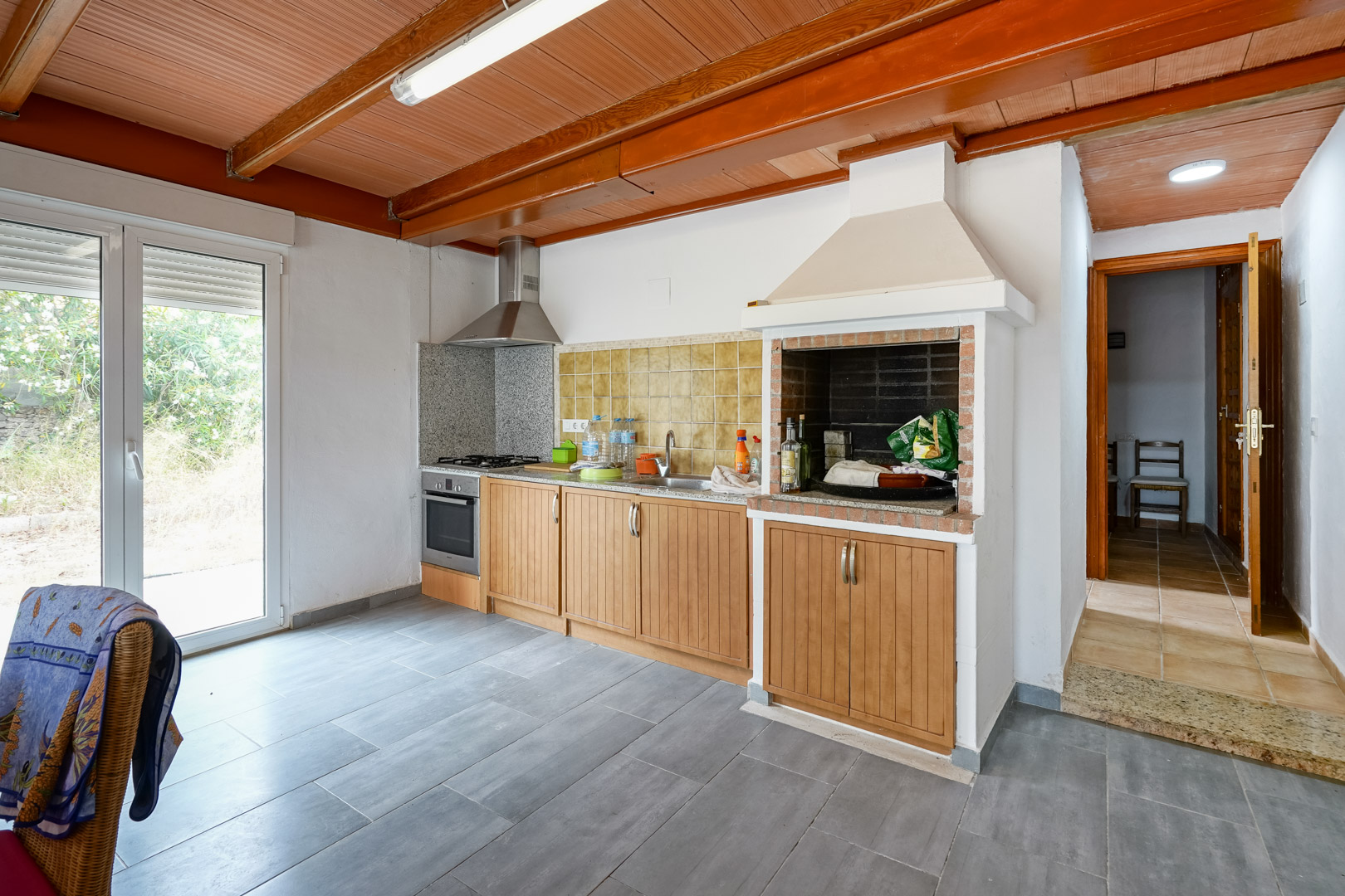 Functional kitchen featuring a wood-paneled ceiling with beams, an integrated brick barbecue, granite countertops, and direct access to the garden.