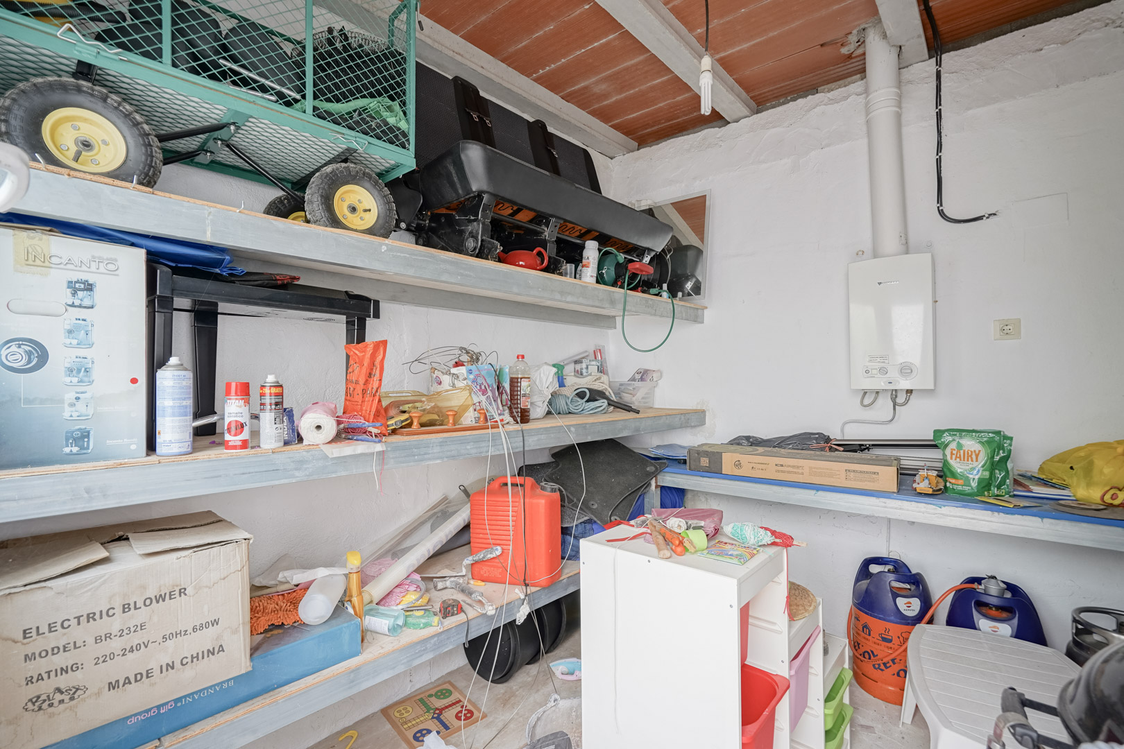 Functional storage room featuring built-in shelving, a wall-mounted gas water heater, and a traditional ceiling with wooden beams and terracotta tiles.