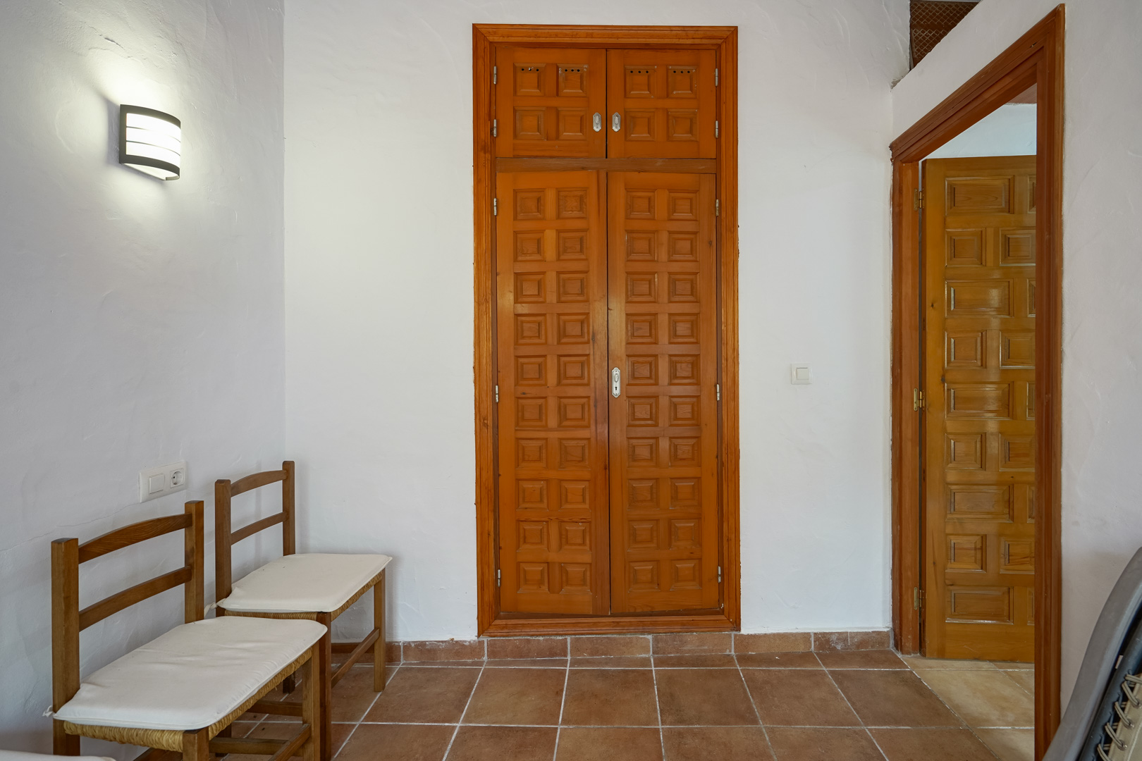 Hallway featuring rustic terracotta tile flooring, white textured walls, and built-in wooden wardrobes with traditional paneled doors and matching trim.
