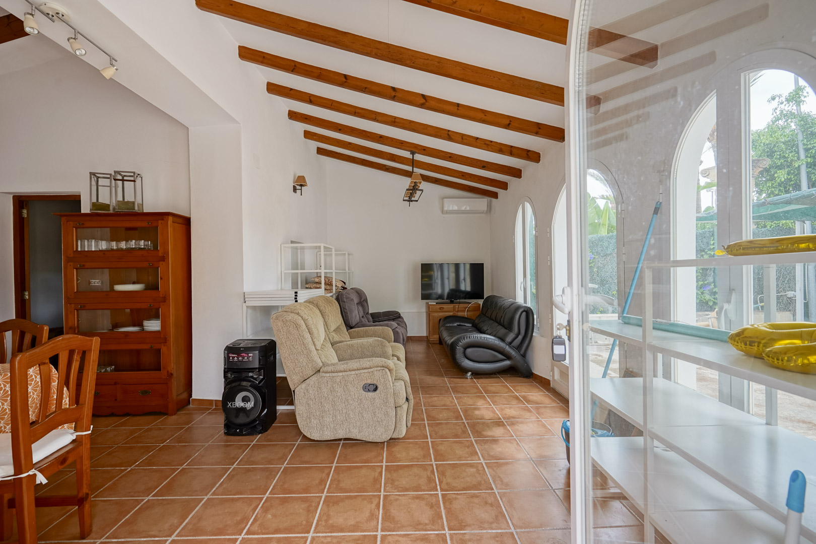 Living area featuring exposed wooden ceiling beams, rustic terracotta floor tiles, and arched windows providing natural light.