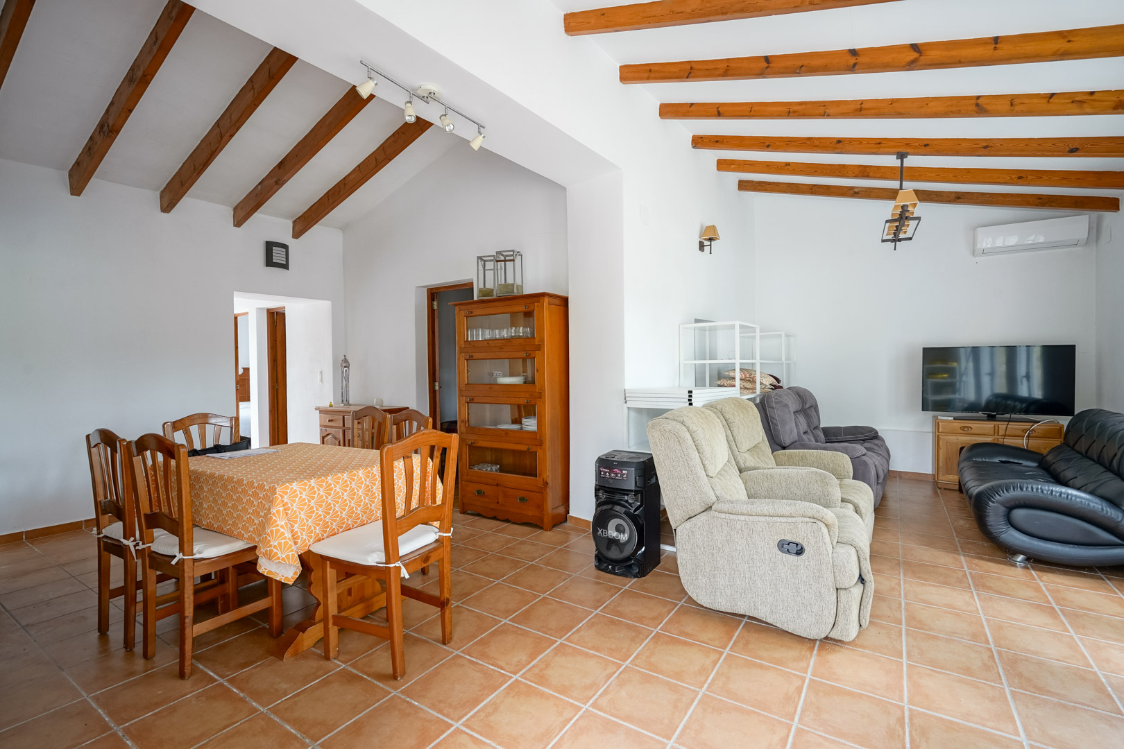 Open-plan living and dining area featuring traditional exposed wooden ceiling beams, terracotta floor tiles, and classic wooden furnishings.