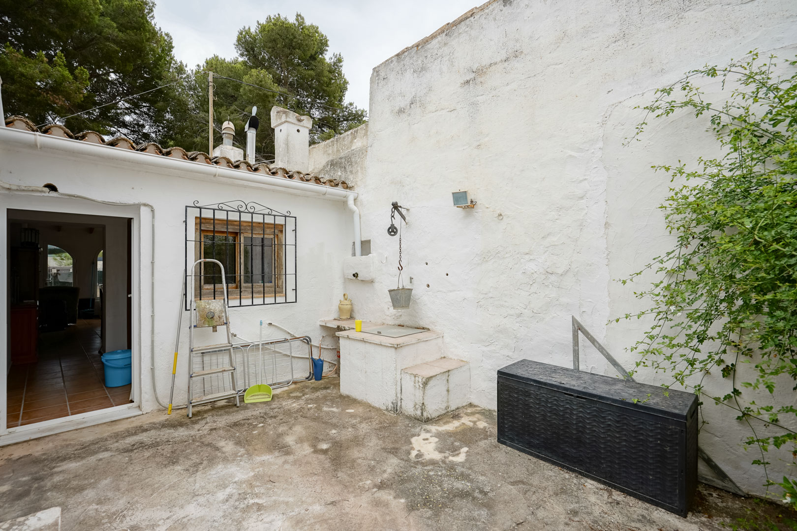 Outdoor patio featuring a traditional well with a pulley system, whitewashed walls, and a tiled roof overlooking the surrounding pine forest.