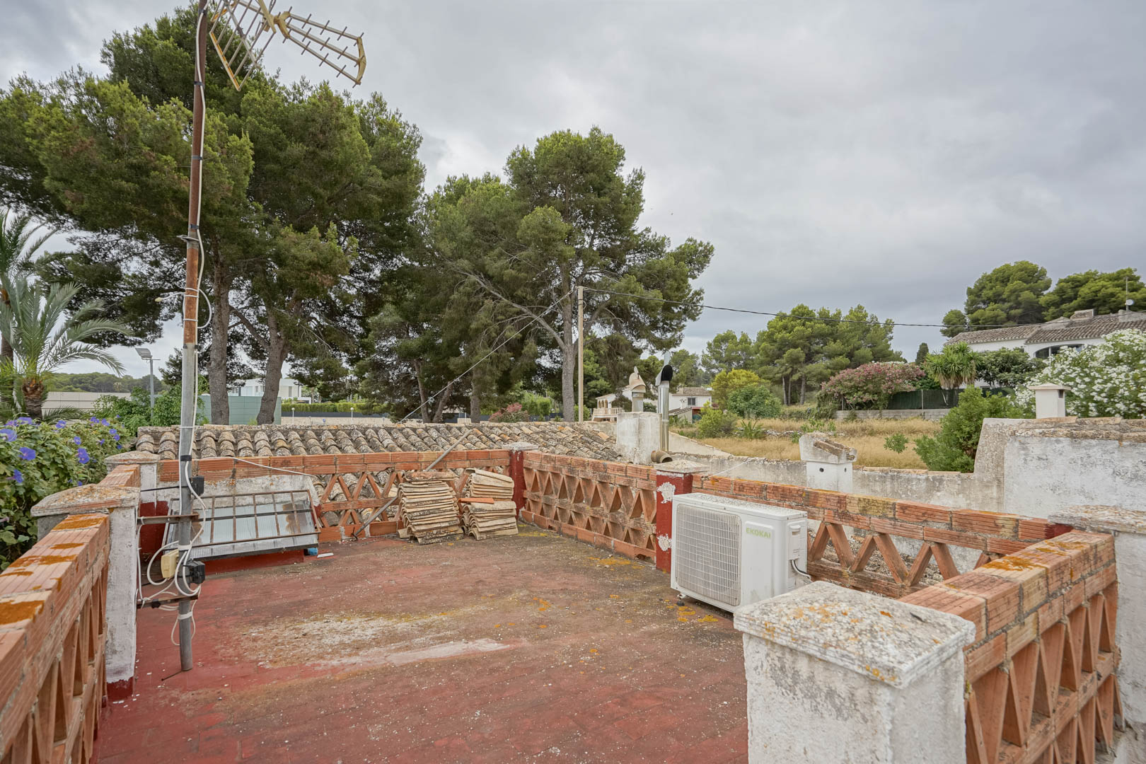Rooftop terrace featuring red tile flooring and decorative brick balustrades. The space provides views of mature pine trees and the surrounding residential area.