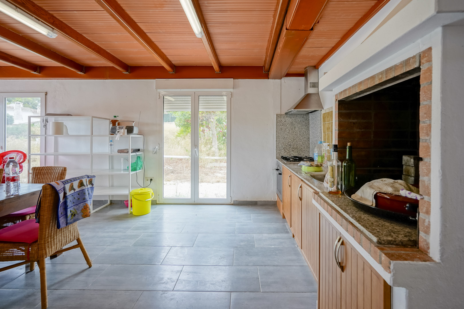 Rustic kitchen featuring wooden ceiling beams, granite countertops, and a built-in brick barbecue, with direct garden access through double glass doors.