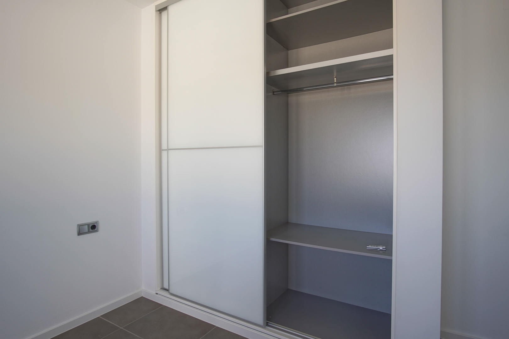 Built-in wardrobe featuring white sliding doors and a gray interior with organized shelving and a hanging rail in a minimalist room.