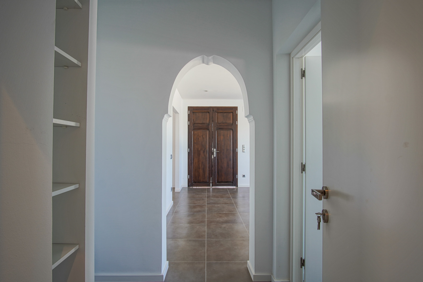 Interior hallway featuring a Mediterranean-style archway framing a restored dark wood double door and earthy-toned ceramic floor tiles.