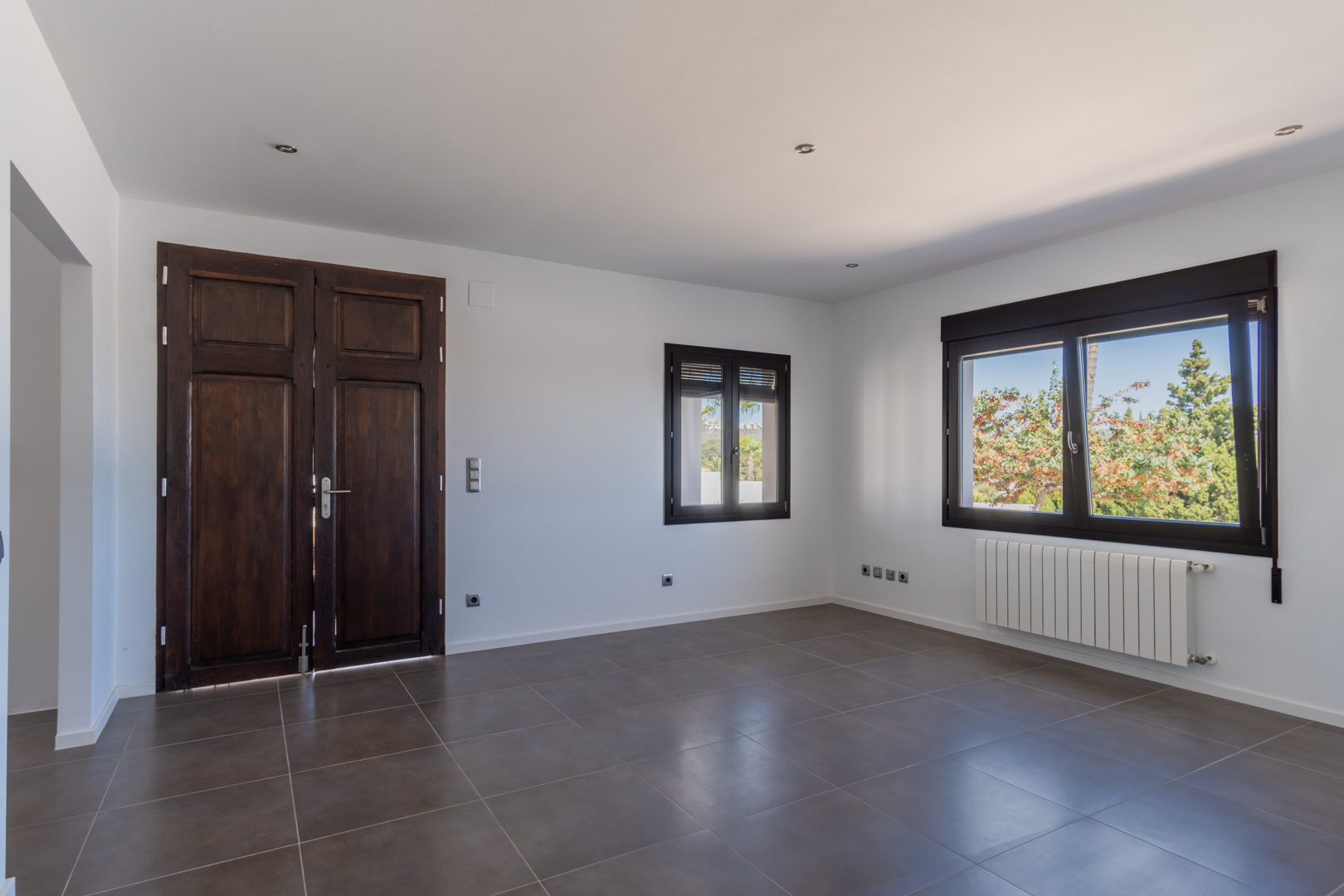 Living space featuring a restored antique wooden door, wood-effect aluminum windows, radiator heating, and large-format grey ceramic floor tiles.