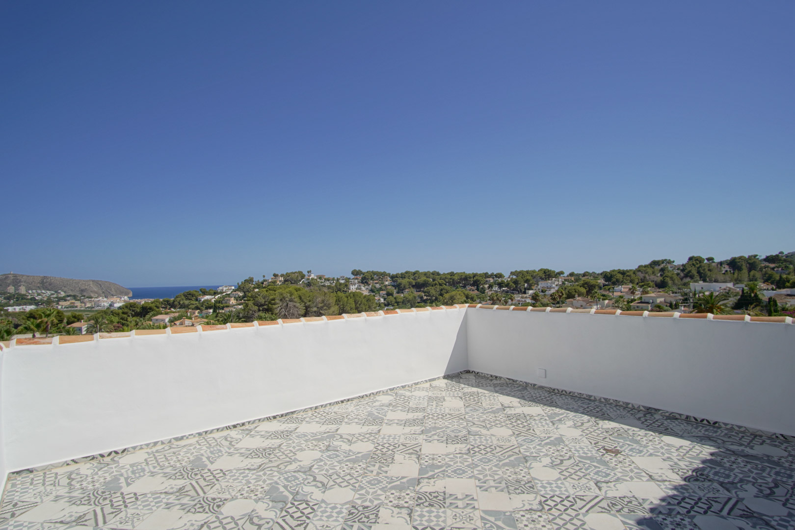 Rooftop solarium featuring patterned ceramic floor tiles and white perimeter walls, offering panoramic views of the Mediterranean Sea and Moraira coastline.