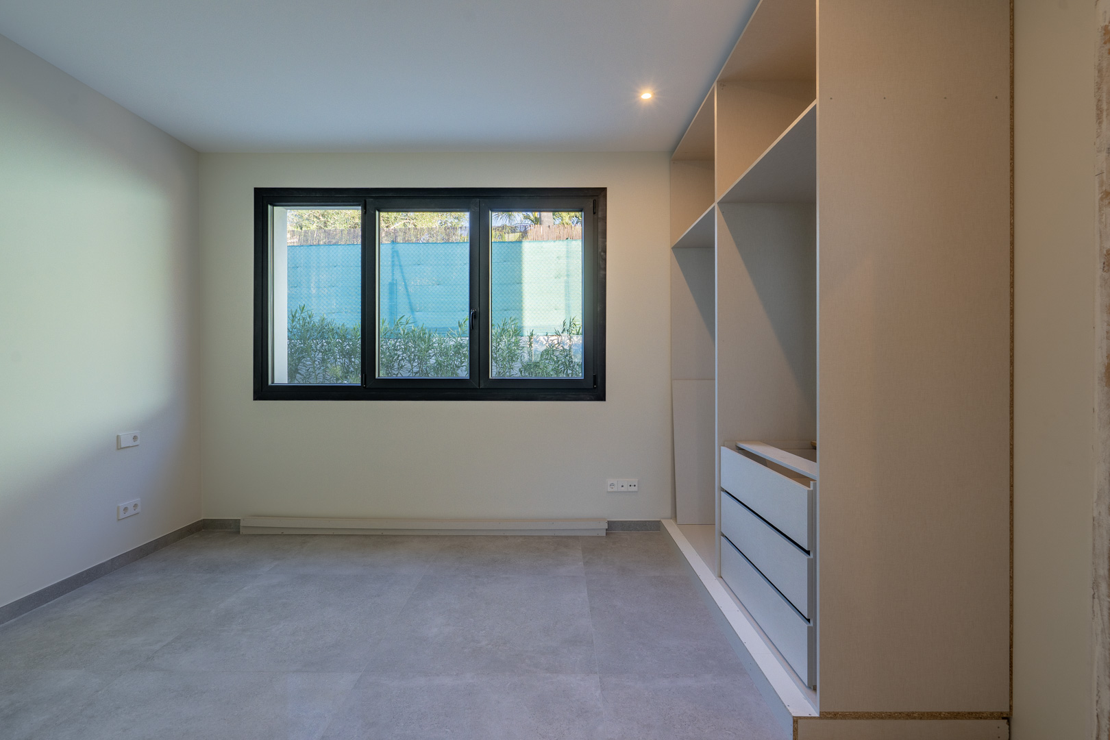 Bright bedroom with a triple-pane window and a built-in wardrobe without doors. Gray tiled floor.