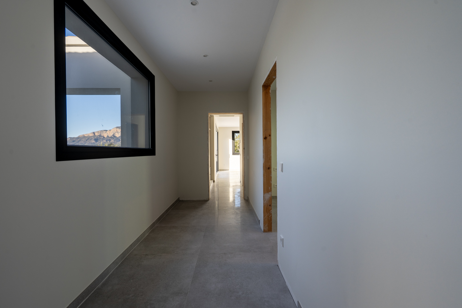 Bright hallway with gray tile flooring and a mountain view through a rectangular window with a black frame.