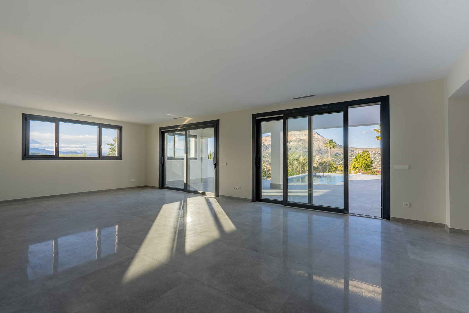 Expansive living room featuring gray tiled flooring and large windows with views of the pool and landscape.
