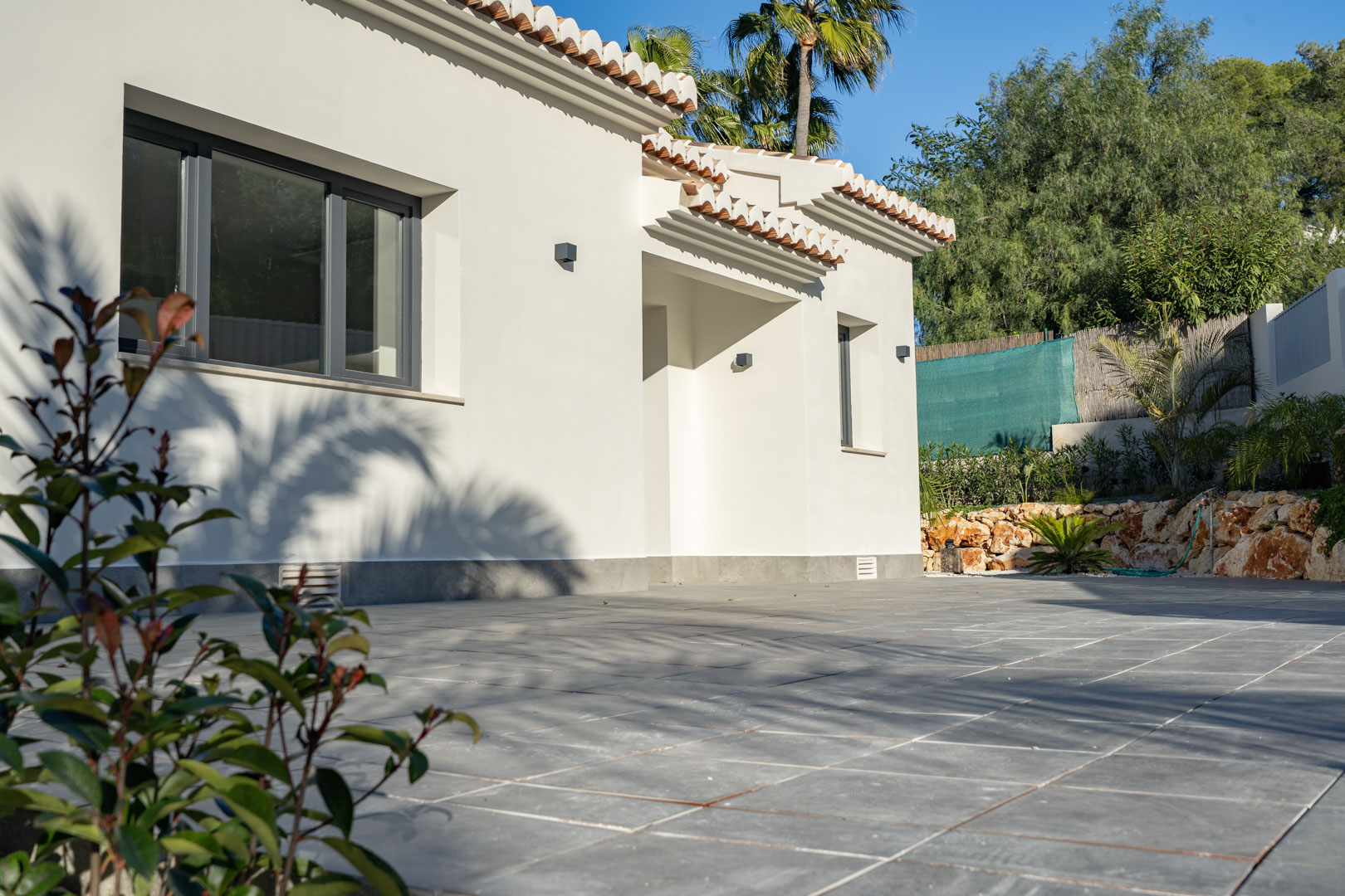 Exterior view of the villa featuring a white facade, terracotta roof tiles, and gray tiled flooring.