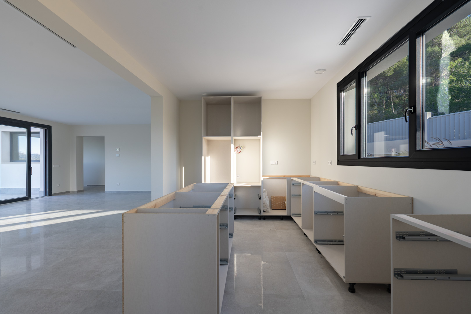 Kitchen under construction with white cabinet bases and gray tile floor. Window with black trim.