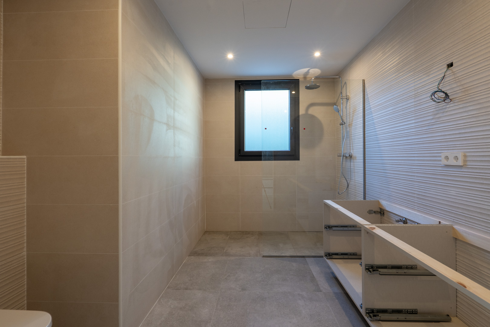 Modern bathroom detail featuring a shower, square window, and unfinished vanity.