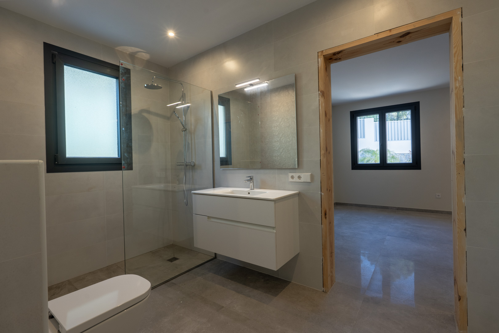Modern bathroom detail: glass-enclosed shower, floating vanity, and window with diffused light.
