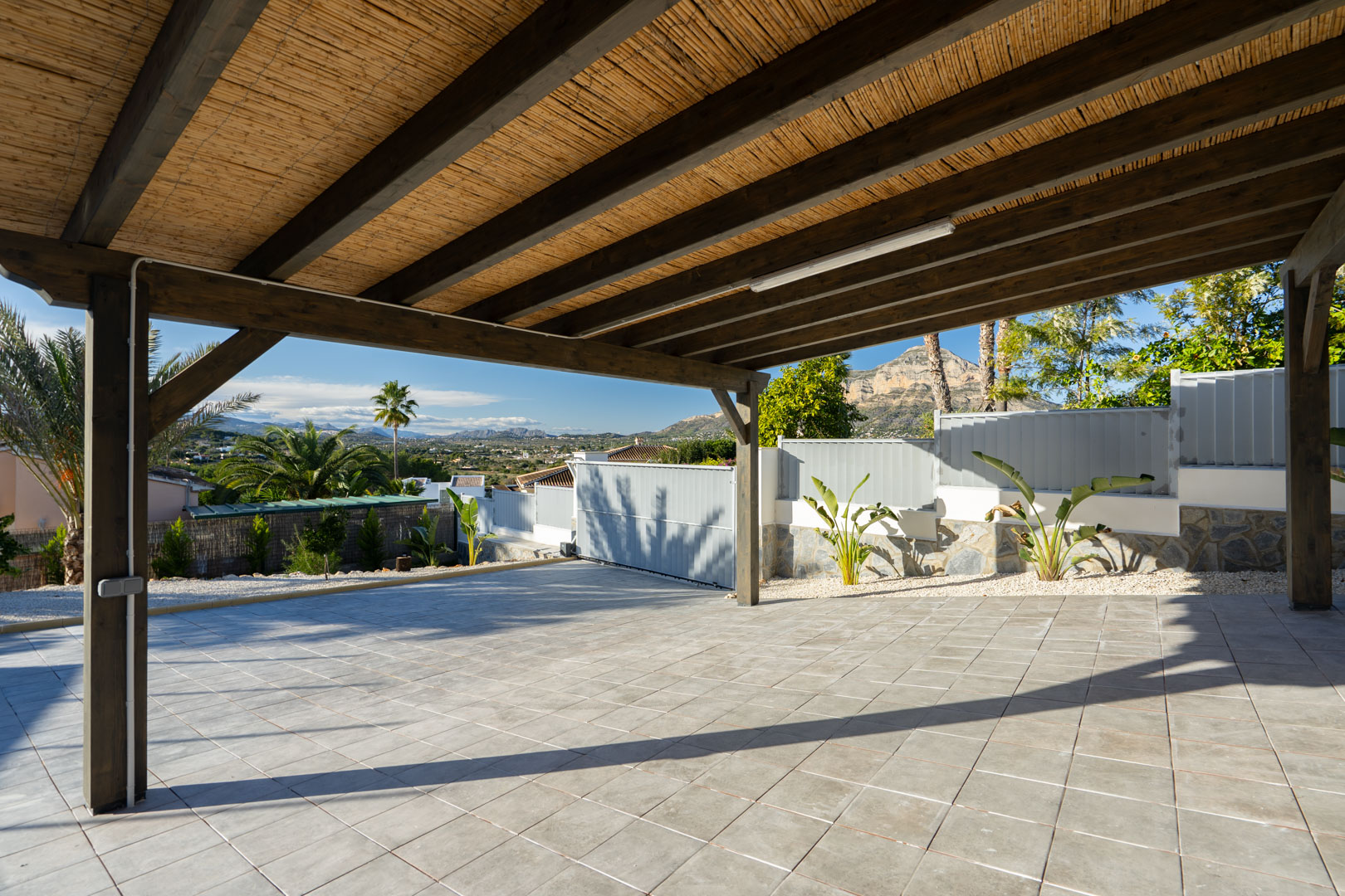 Pergola with reed ceiling and tiled floor, overlooking greenery and mountains.