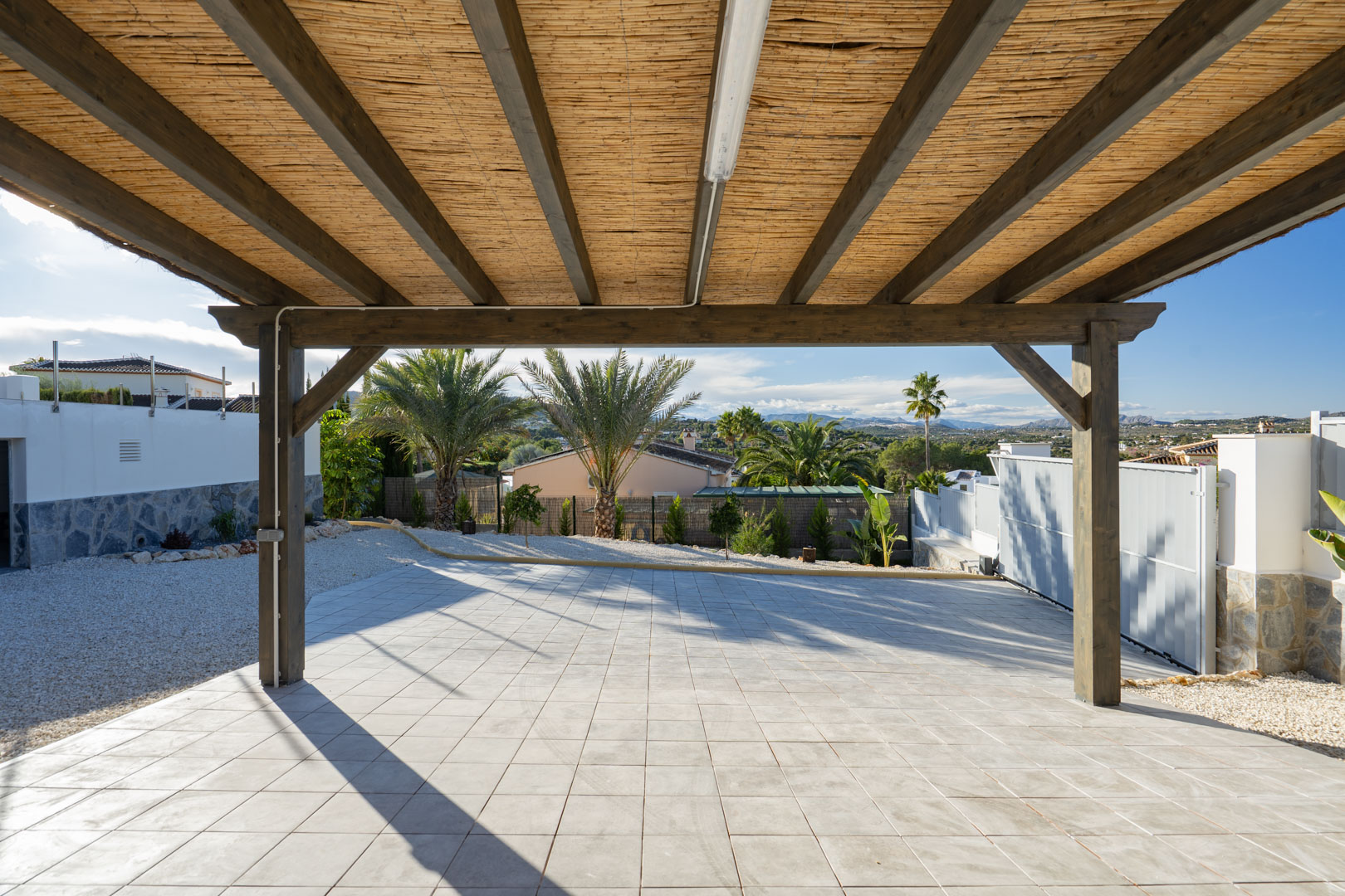 Pergola with wood structure and reed cover, over tiled floor in Jávea villa.