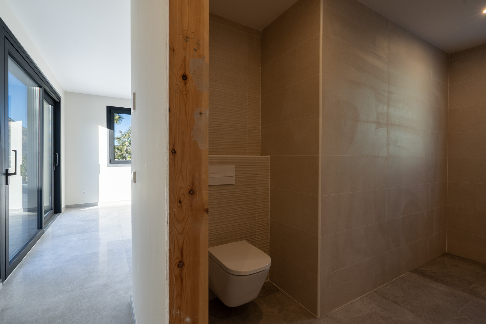 Powder room detail with sand-colored tiles and an unfinished wood door frame, overlooking the hallway.
