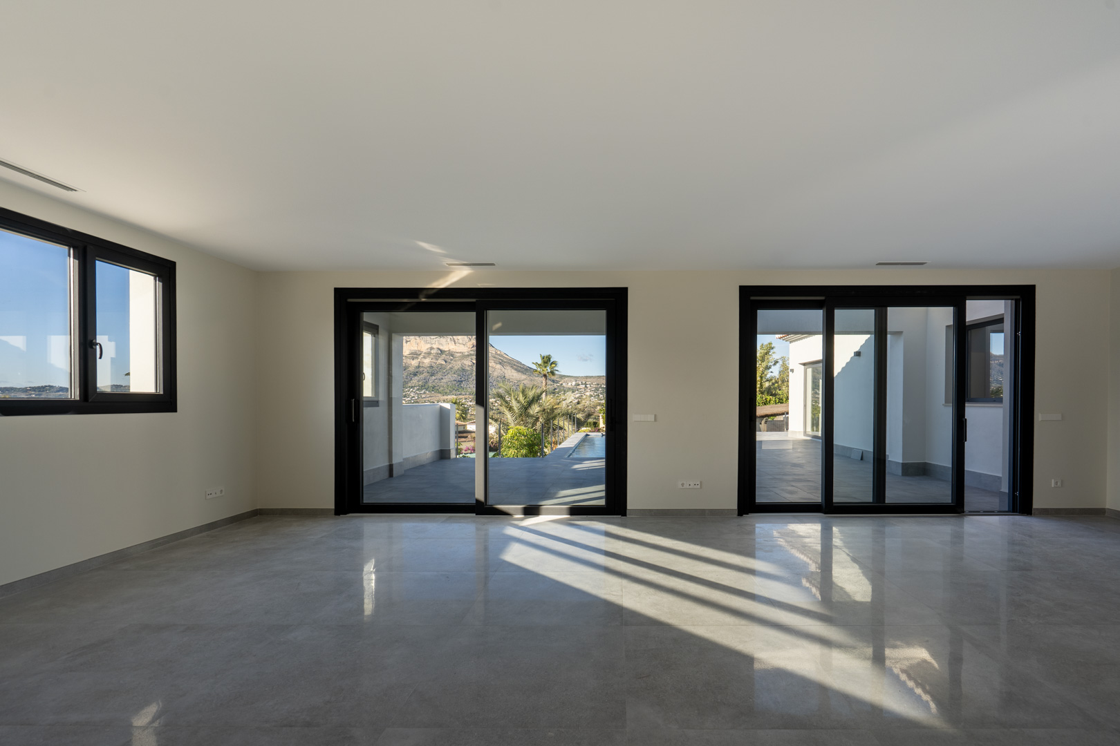 Spacious living room featuring gray tiled flooring and expansive sliding glass doors with black frames.