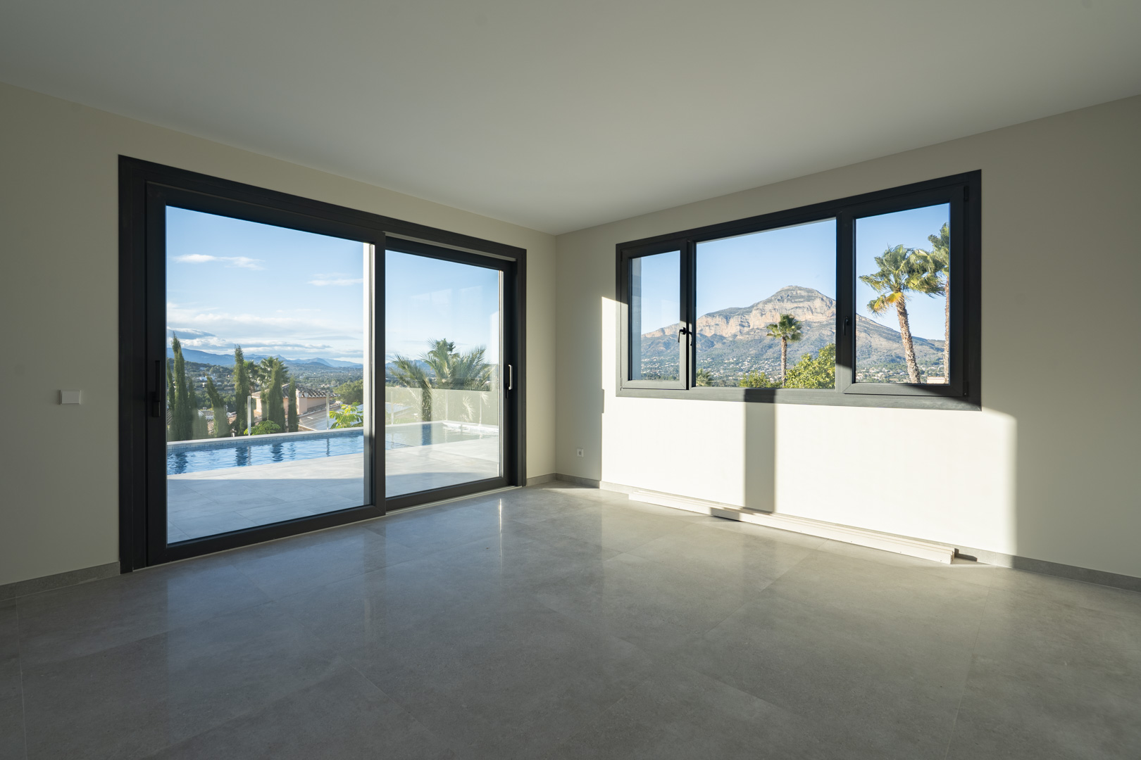 Spacious living room featuring gray tiled flooring and large windows offering views of the pool and mountain landscape.