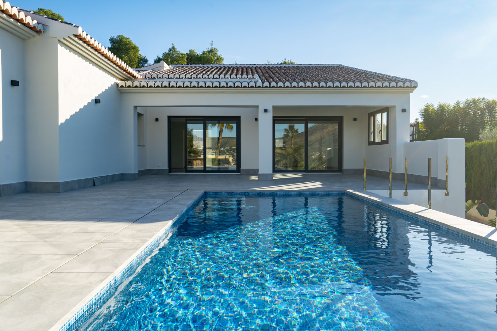 View of the private pool with blue mosaic tiles and the villa's grey tiled terrace.