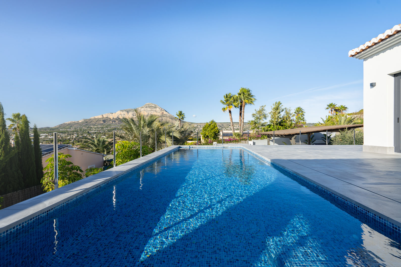 View of the private pool with blue tiles, grey tiled terrace, and mountain views in Jávea.