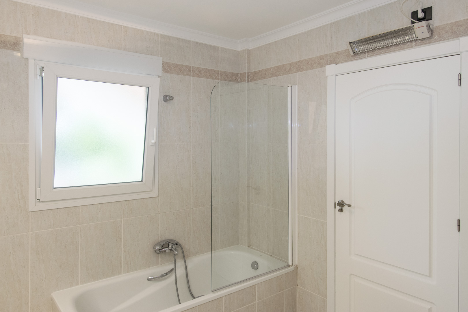 Bathroom featuring a bathtub with a fixed glass screen, ceramic wall tiles with a decorative border, a frosted PVC window, and a wall-mounted heater.