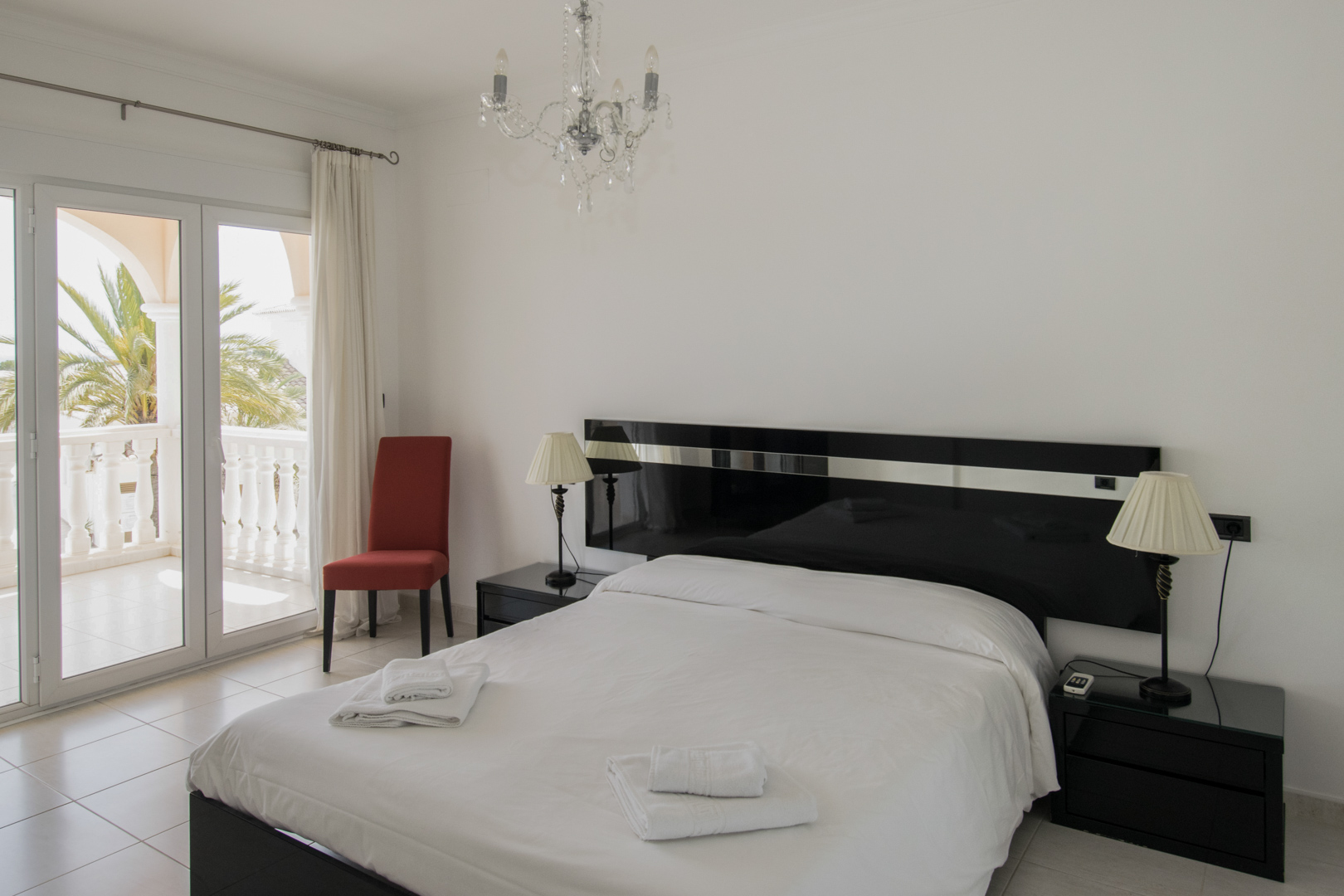 Bedroom featuring a black lacquered headboard, crystal chandelier, and glass doors opening to a private terrace with palm tree views.