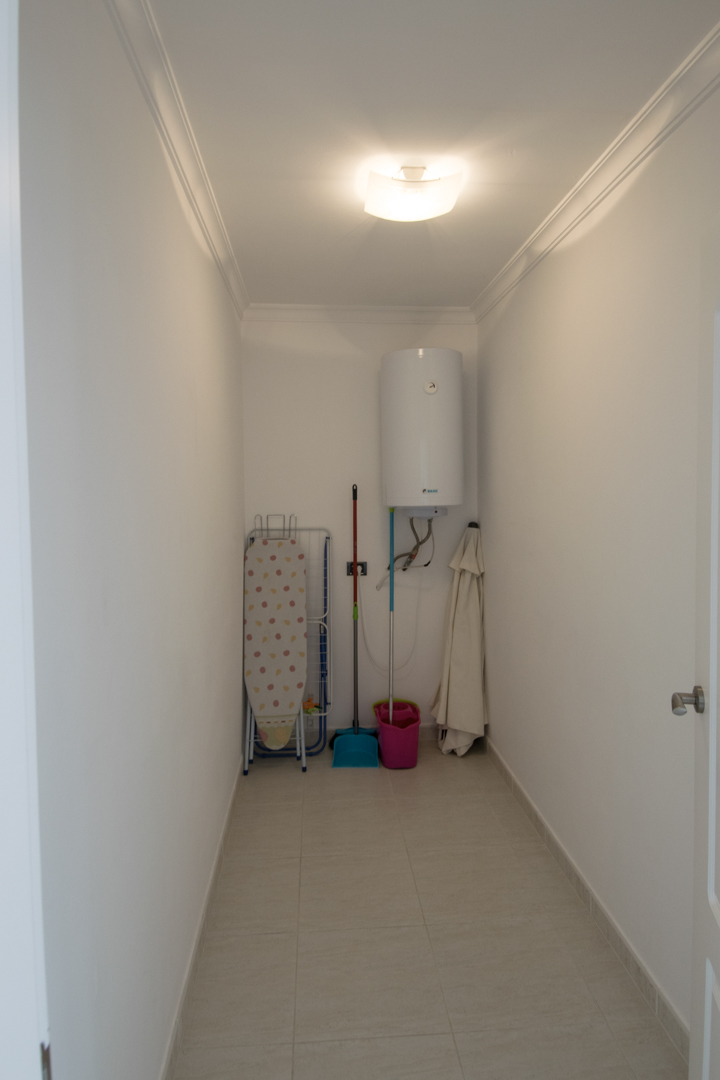 Functional utility room featuring an electric water heater, storage space for cleaning supplies, and tiled flooring with elegant crown molding.