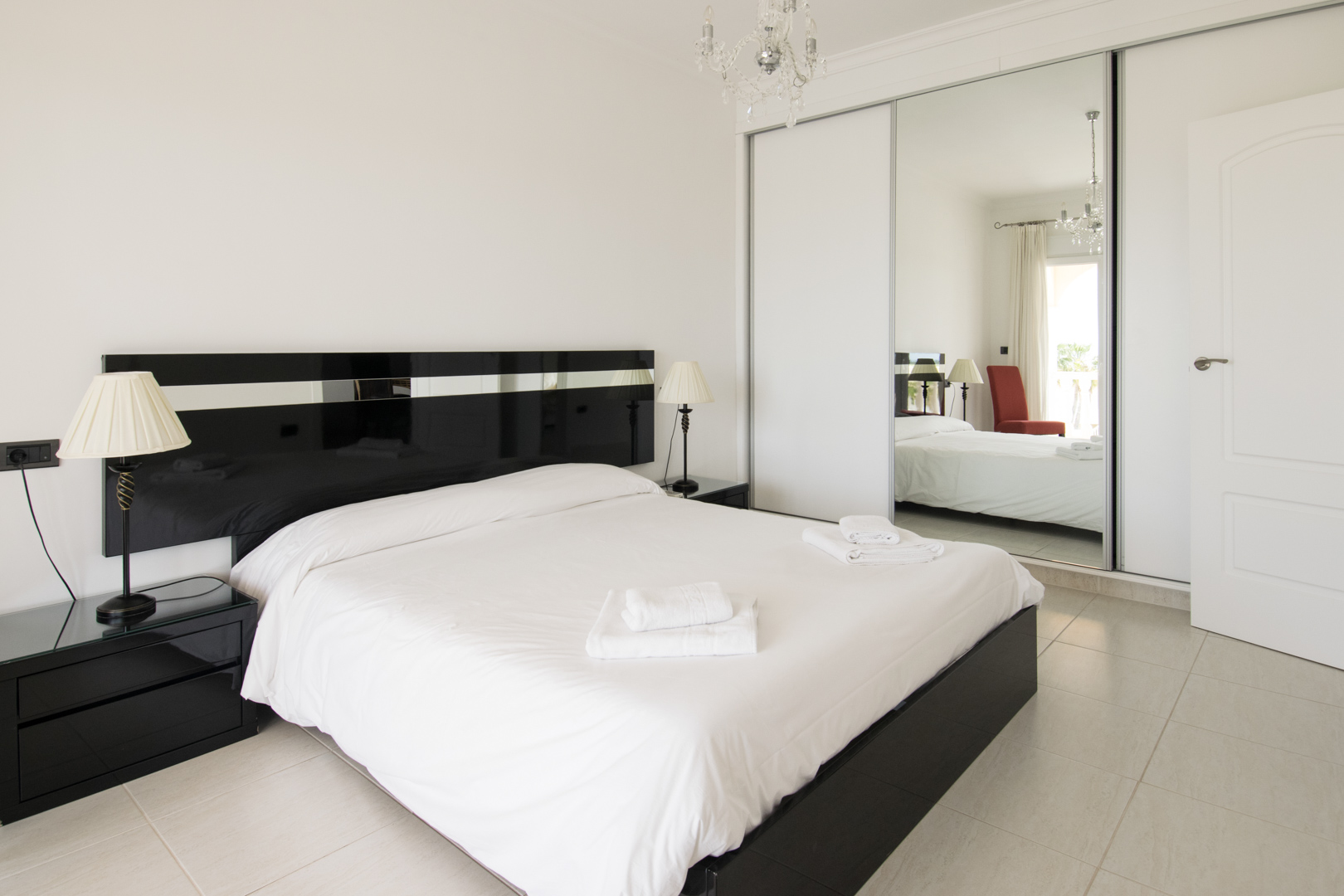 Master bedroom featuring a black lacquered headboard, matching nightstands, and a large built-in wardrobe with sliding mirrored doors and crystal chandelier lighting.