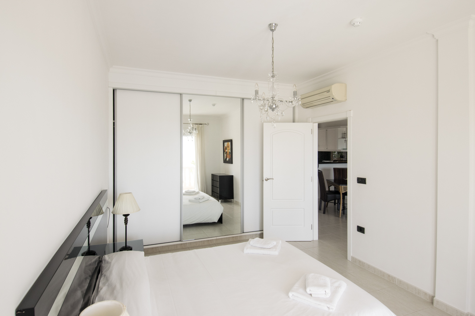 Master bedroom featuring a built-in wardrobe with mirrored sliding doors, a crystal chandelier, and integrated air conditioning above the doorway.