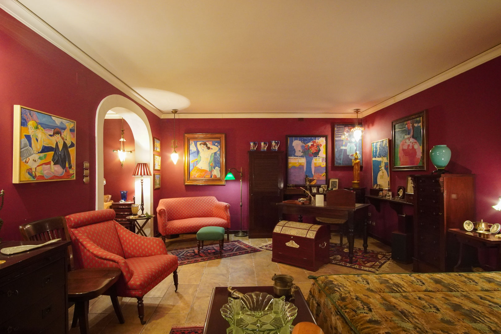 Classic living area featuring deep burgundy walls, marble flooring, and an integrated study. The space is decorated with fine art, period furniture, and warm ambient lighting.