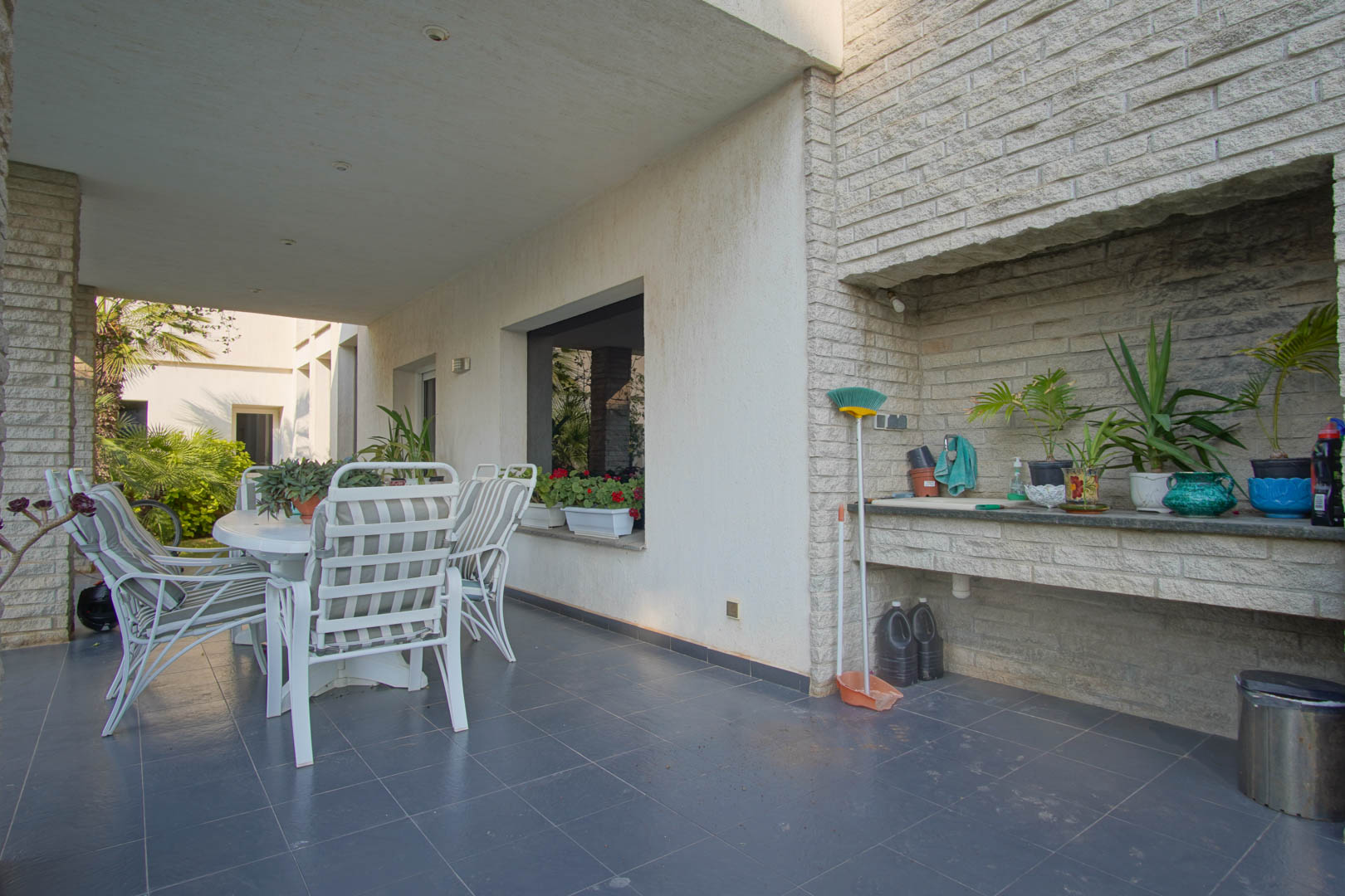 Covered terrace featuring dark tiled flooring, an outdoor dining set, and a built-in stone summer kitchen with a functional sink and countertop.