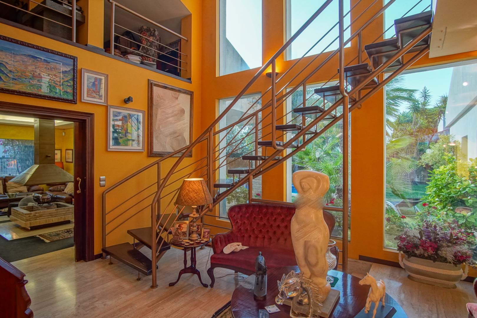 Double-height living space featuring an open-tread staircase, large vertical windows with garden views, and polished marble flooring.