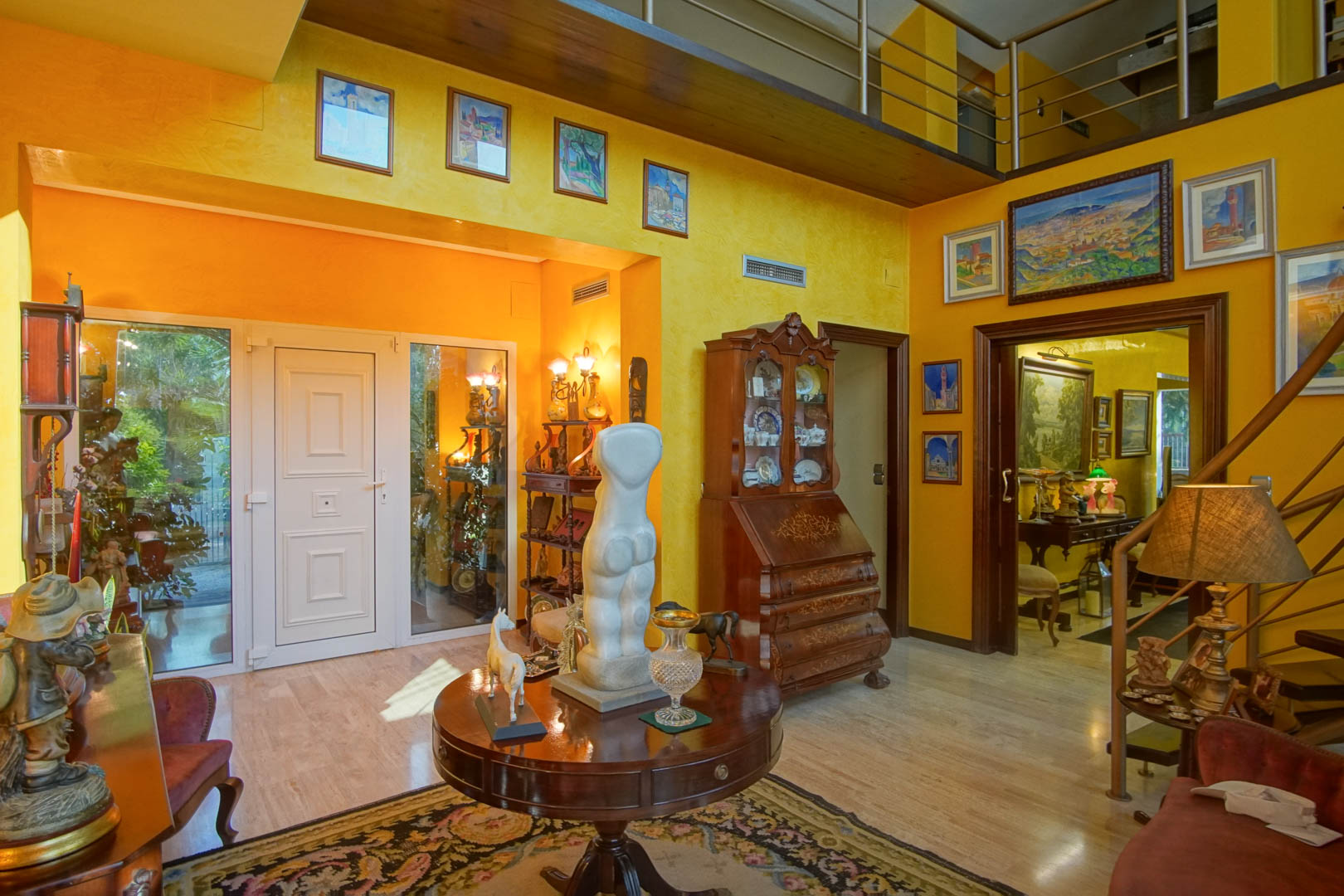 Entrance hall featuring marble flooring, ochre walls, and a double-height ceiling with a wood-paneled mezzanine and metal railing.