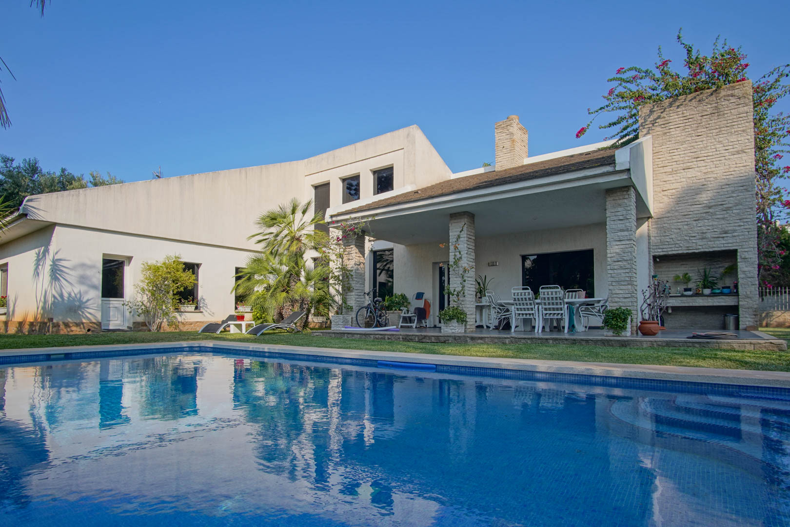 Exterior view featuring the private swimming pool and covered terrace with stone pillars, outdoor dining area, and integrated barbecue station.