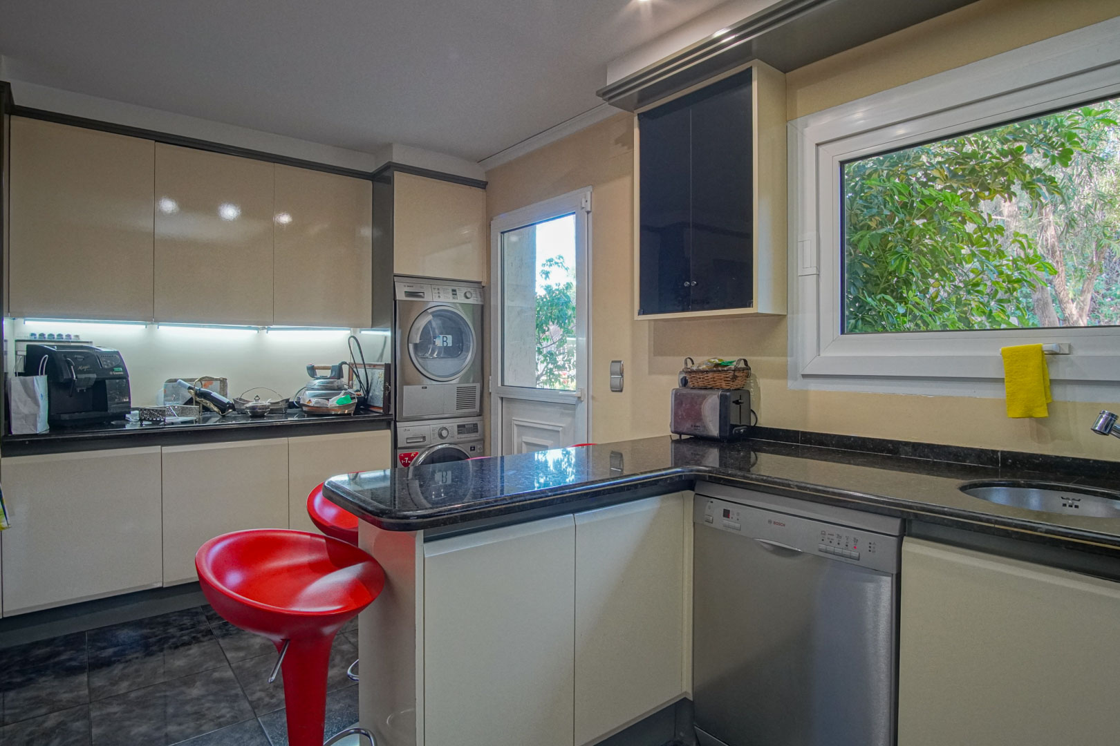 Fully equipped kitchen featuring dark granite countertops, integrated appliances, a laundry station, and a breakfast bar with red stools. Includes direct outdoor access.