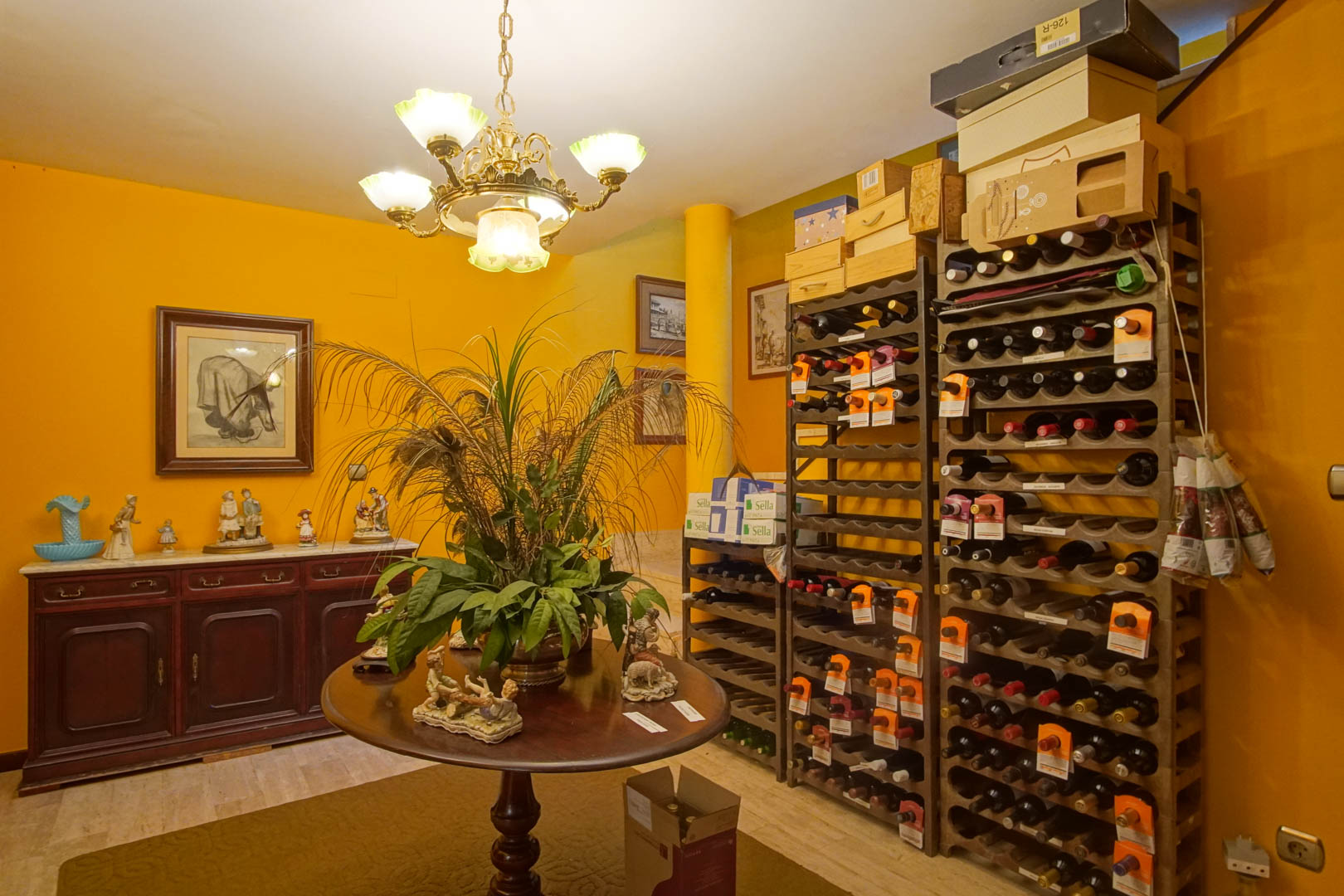 Interior wine cellar featuring vertical bottle racks, a central wooden table, and a classic sideboard against ochre walls and marble flooring.