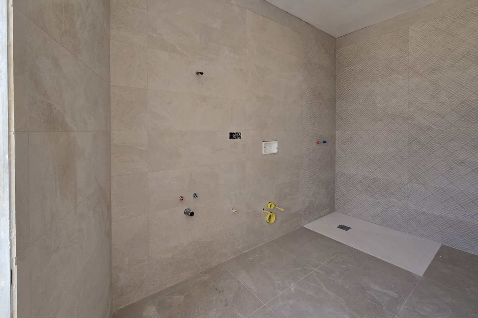 Bathroom under construction featuring sand-toned porcelain tiles, a geometric textured accent wall in the shower, and a white low-profile shower tray.