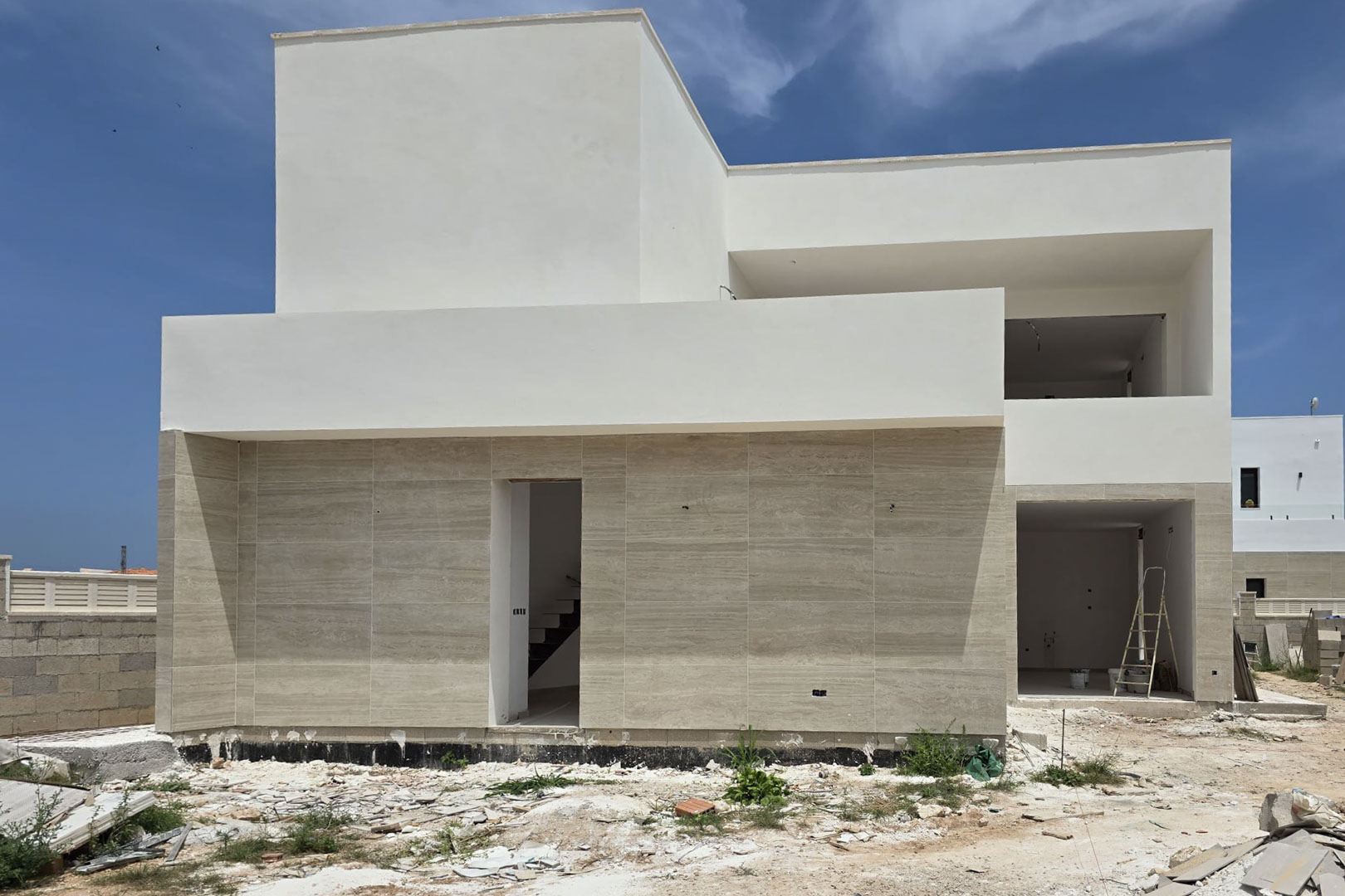 Exterior facade of the villa under construction featuring a minimalist design with light stone cladding on the ground floor and white finishes on the upper level.