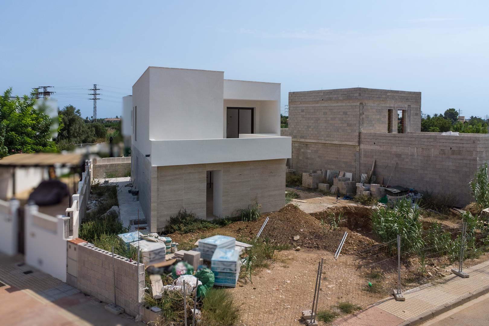 Exterior view of the villa under construction featuring stone cladding on the ground floor and a white upper level. The site includes the pool excavation.